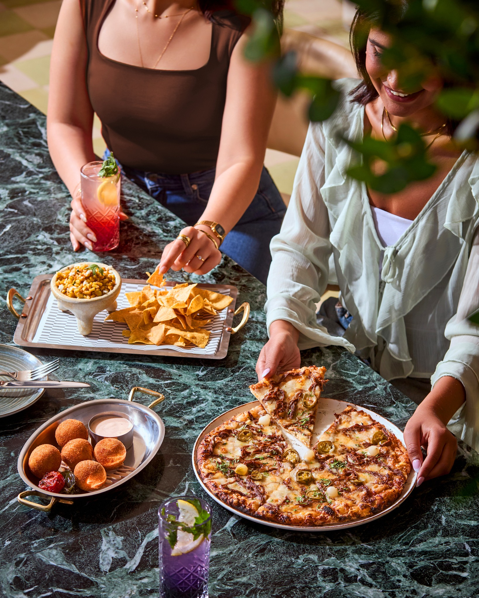 Friends sharing pizza and mocktails on a green marble table