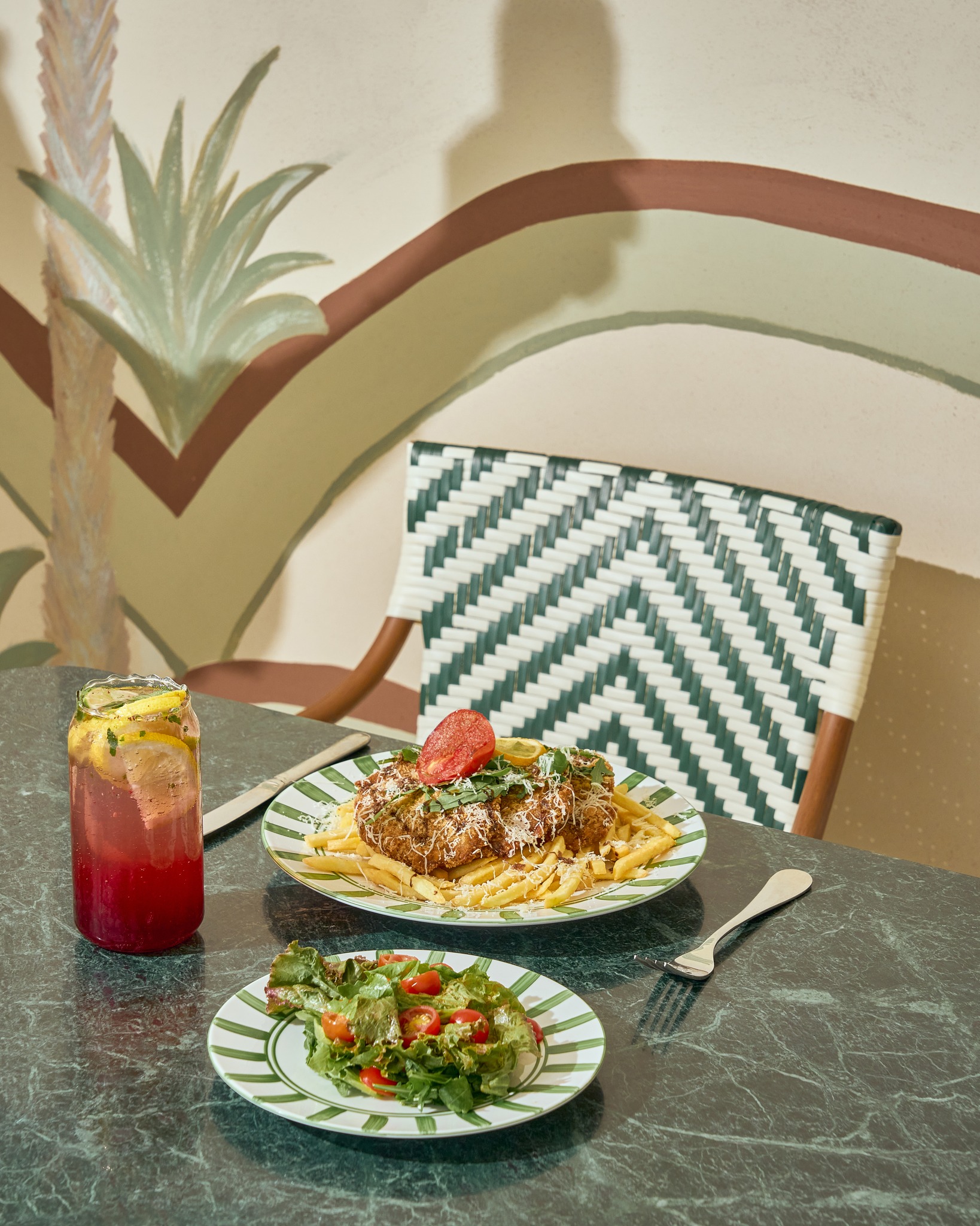 Crispy chicken with fries and a side salad against a painted palm mural
