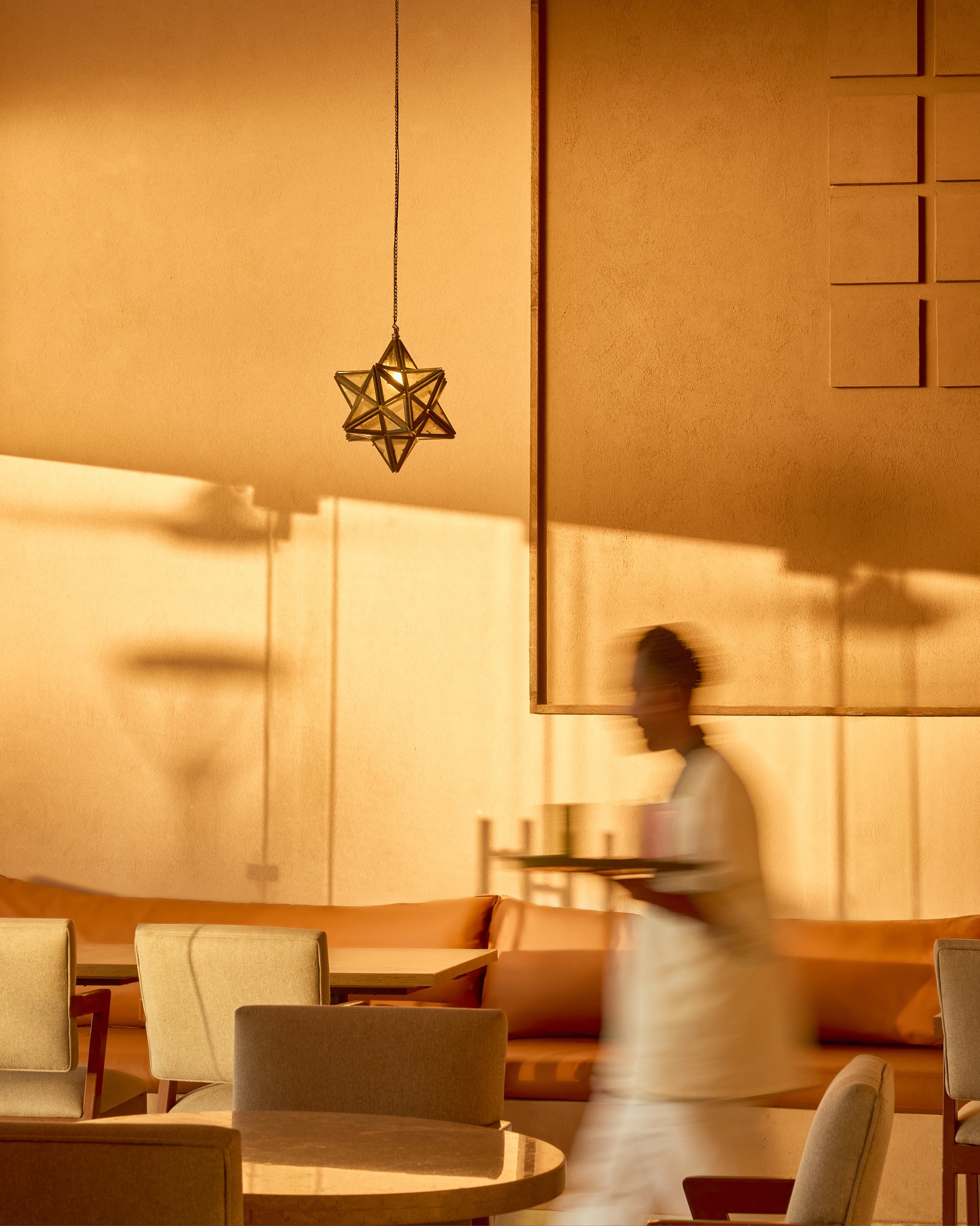 Star pendant lamp and a server crossing the dining room at golden hour